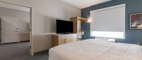 A bedroom with a bed, a television, a wardrobe, and a window with blinds.