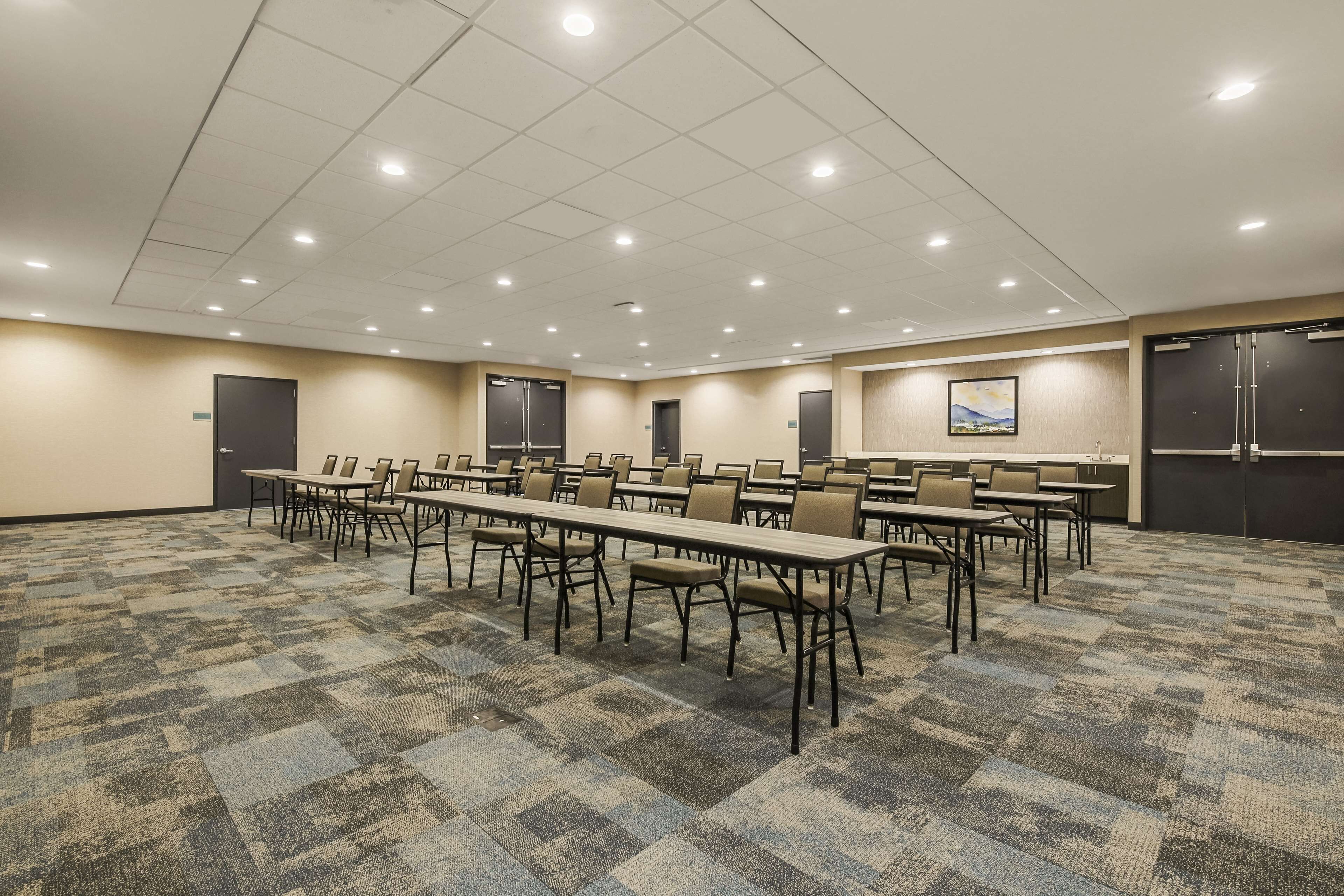 Un salón de conferencias con varias mesas y sillas, suelo alfombrado e iluminación empotrada.