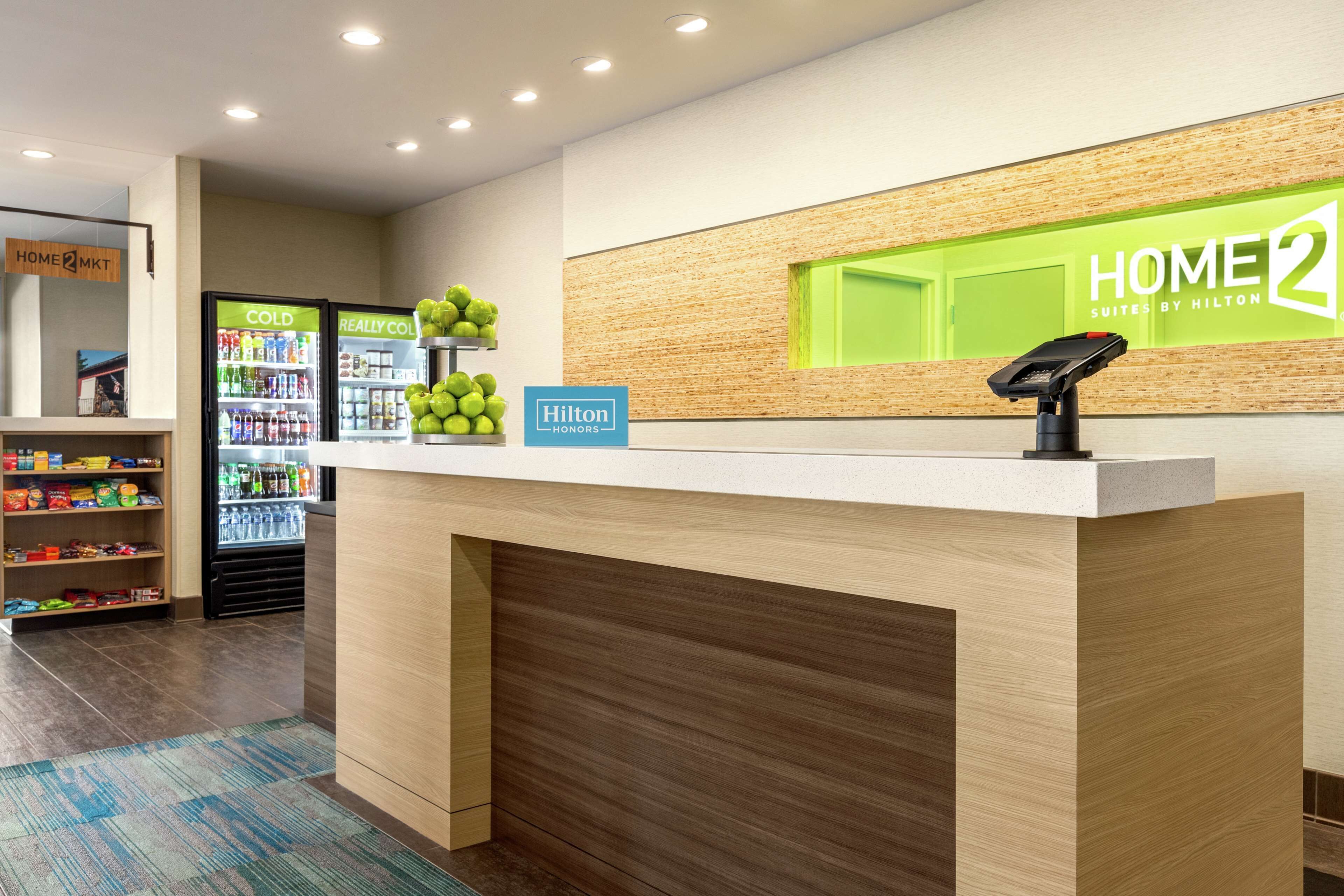 A hotel reception area with a wooden reception desk, a digital kiosk, and vending machines labeled "COLD" and "REALLY COLD".