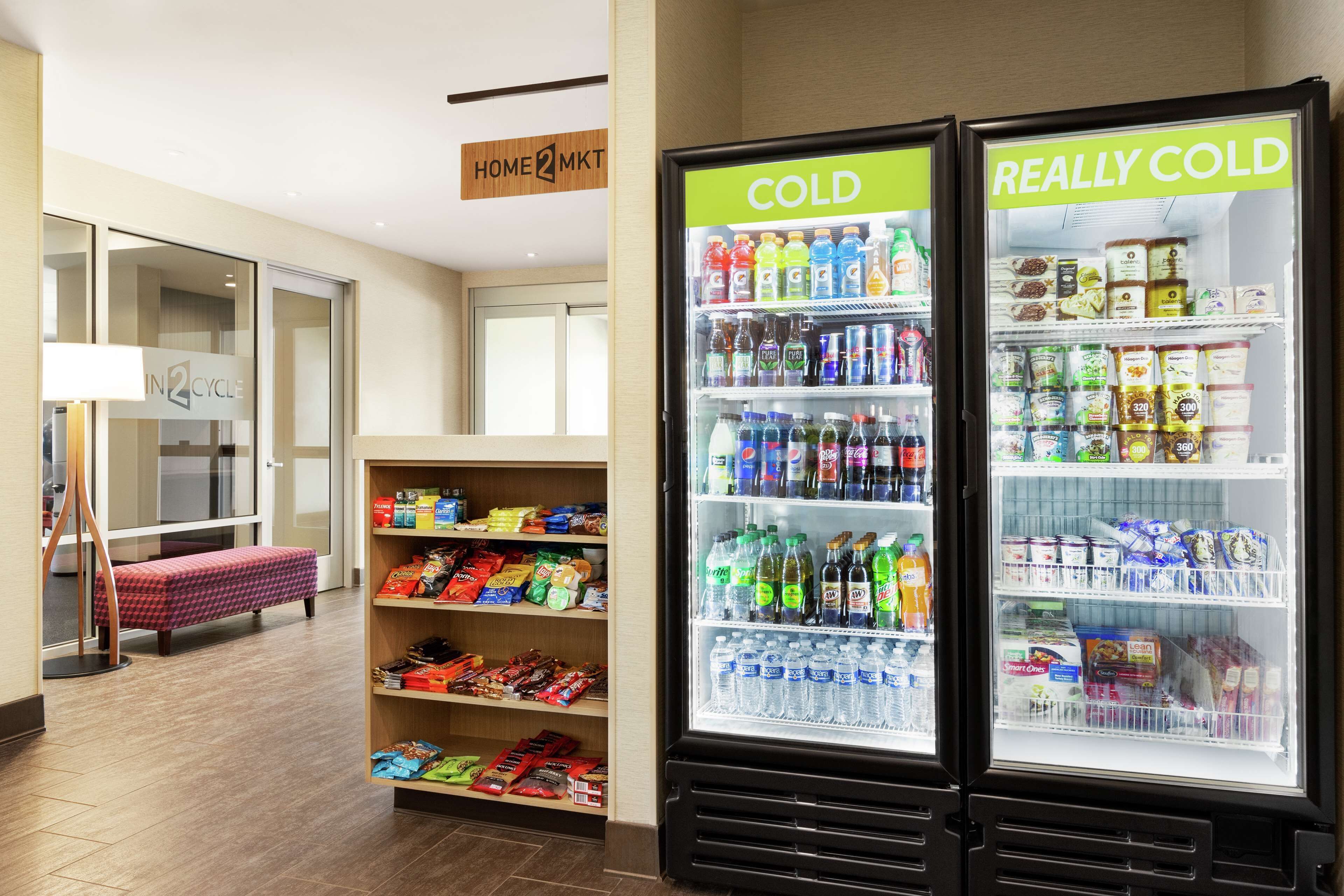 Un hall d’hôtel comprenant un comptoir d’enregistrement, un bureau de réception et deux grands réfrigérateurs à boissons, l’un portant l’inscription « FROID » et l’autre « TRÈS FROID ».