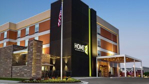 A modern hotel with a prominent "HOME 2 Suites by Hilton" sign, a flagpole with an American flag, and a well-lit entrance area. - Home2 Suites by Hilton Leesburg (Leesburg)