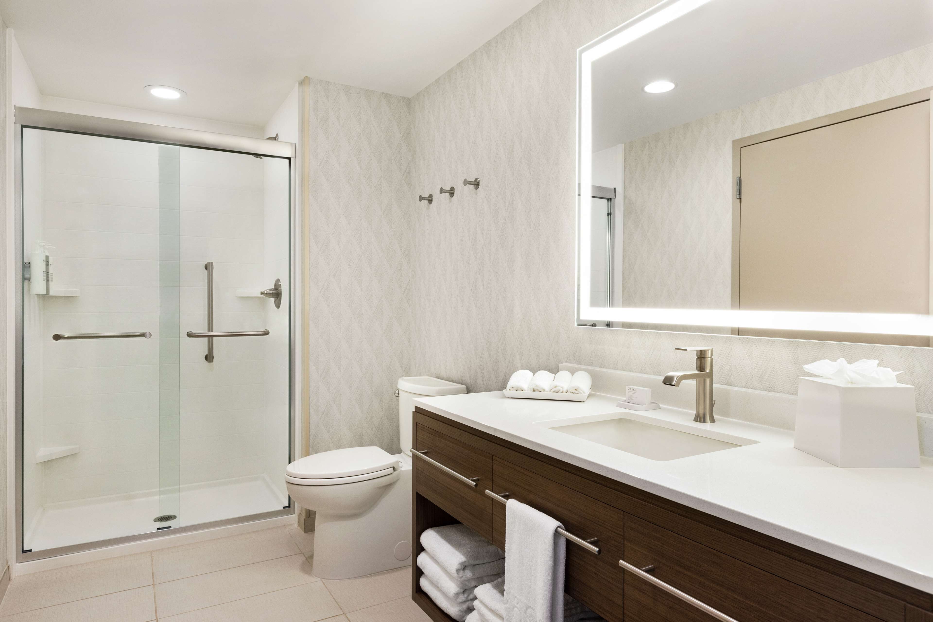 Une salle de bain moderne avec une douche à parois de verre, des toilettes blanches, un meuble-lavabo avec un miroir et un évier.