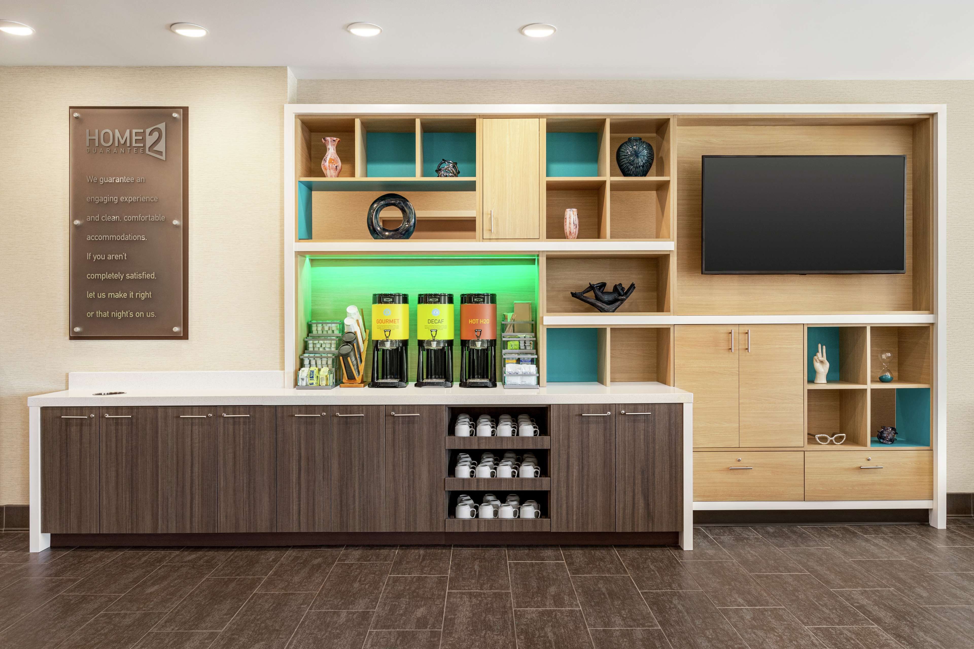 A hotel reception area with a modern design, including a counter with coffee machines, a flat-screen TV, and various decorative items on shelves.