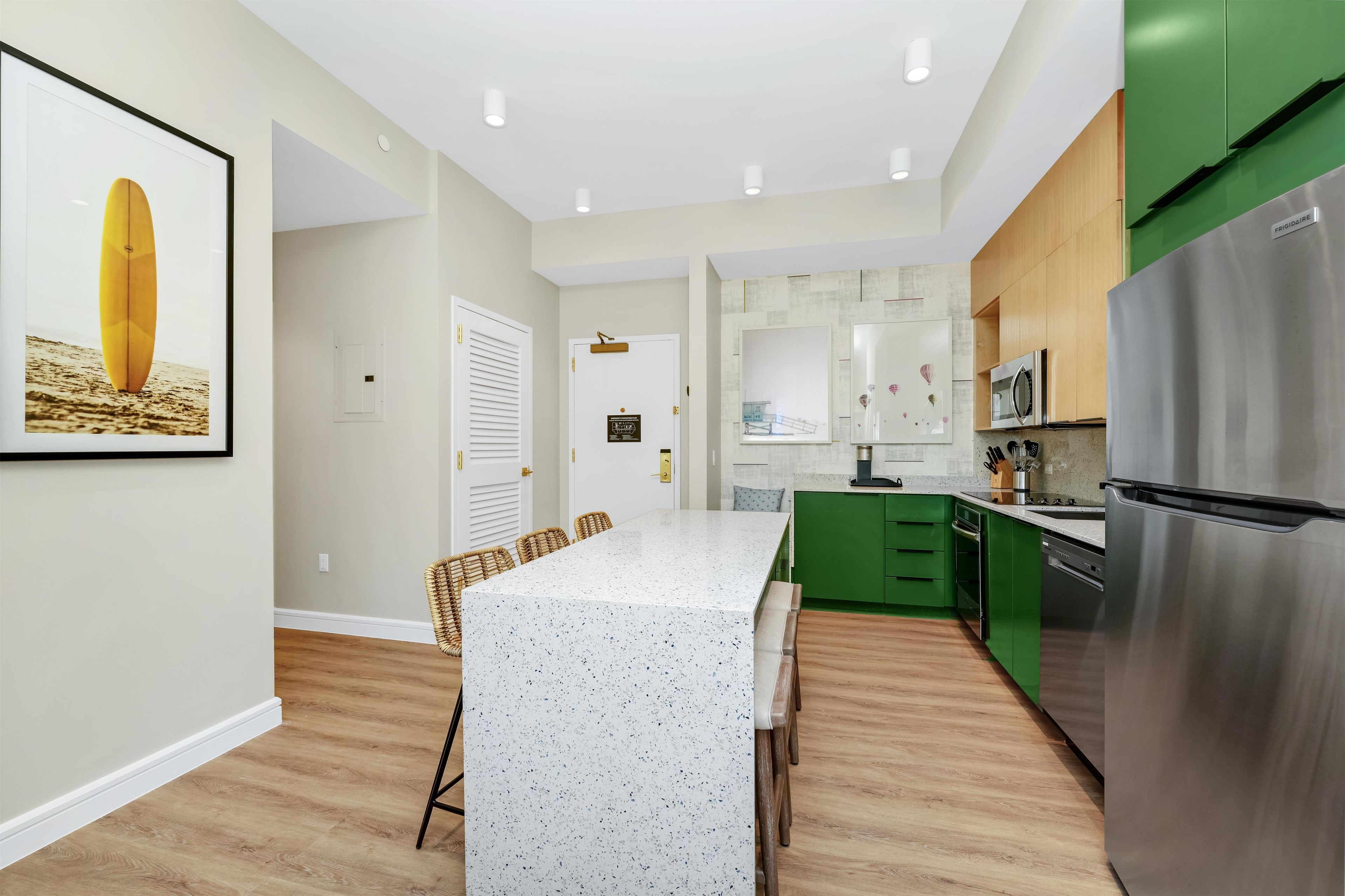 A modern kitchen with a central island, green cabinets, stainless steel appliances, and a framed picture on the wall.