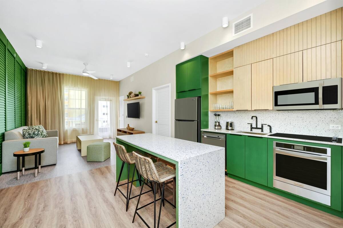 Een moderne keuken met groene kastjes, een wit aanrechtblad en een inbouwoven.