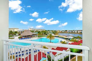 Un resort con una gran piscina, una estructura con techo de paja y vistas del entorno, incluyendo otros edificios y una masa de agua.