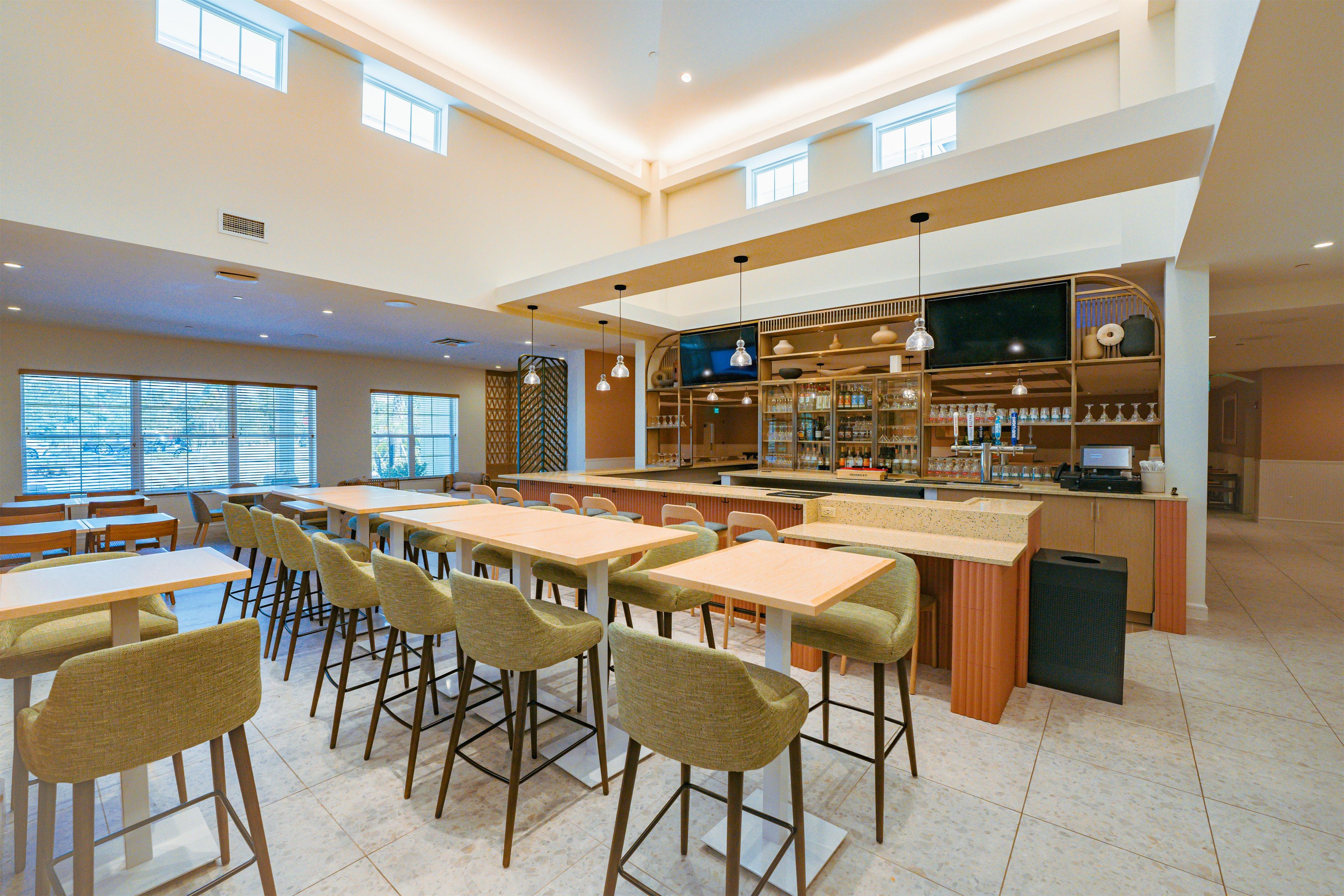 A spacious indoor area with multiple tables and chairs, a bar area with shelves stocked with bottles, and a large flat-screen TV mounted on the wall.
