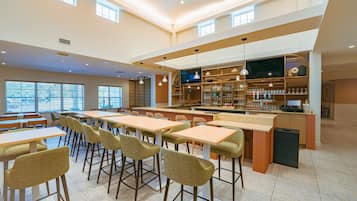 A spacious indoor area with multiple tables and chairs, a bar area with shelves stocked with bottles, and a large flat-screen TV mounted on the wall.
