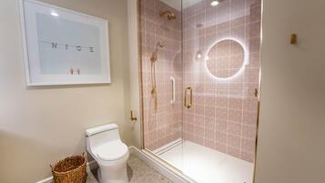 A bathroom with a toilet, a shower with a glass door, and a framed picture on the wall.