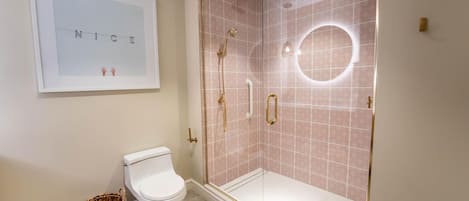 A bathroom with a toilet, a shower with a glass door, and a framed picture on the wall.