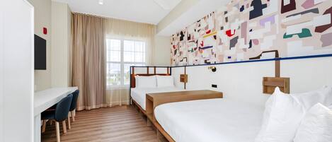 A hotel room with a bed, a desk, two chairs, a ceiling fan, and a large abstract wall art piece.