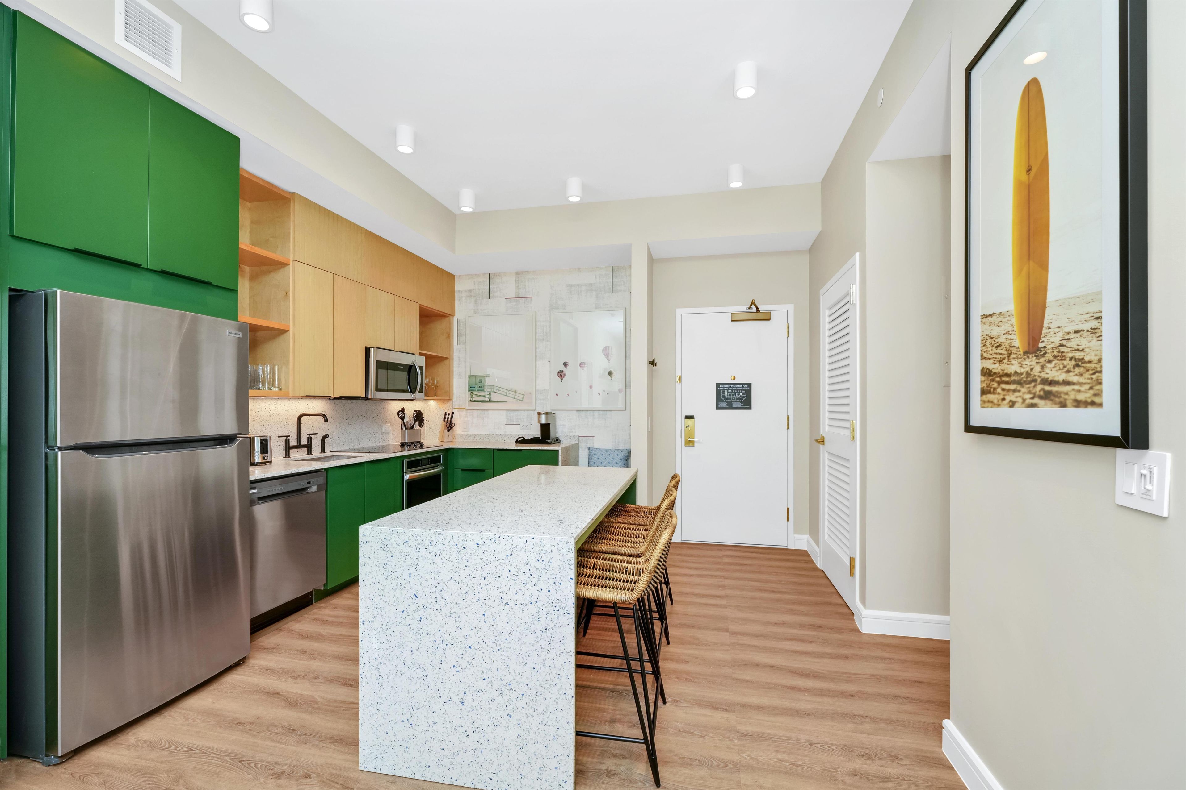 A modern kitchen with green cabinets, stainless steel appliances, and a central island with bar stools.