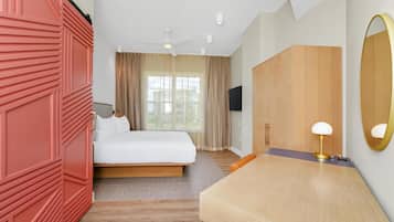 A hotel room with a bed, a desk, a chair, a TV, a ceiling fan, and a large mirror.