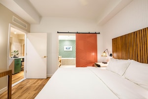 A hotel room with a bed, a desk, a chair, a nightstand, a lamp, and a sliding door leading to a bathroom.