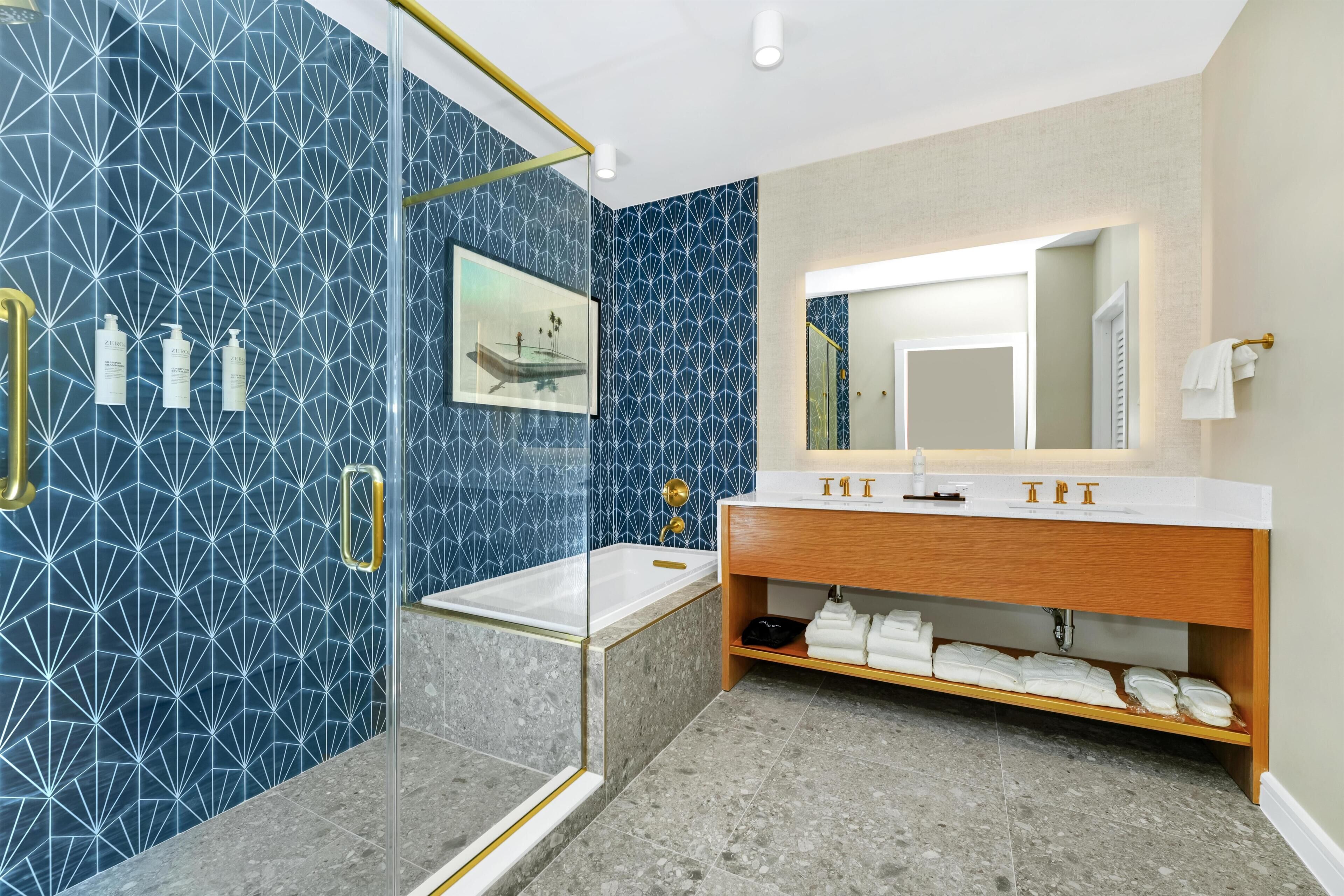 Une salle de bain moderne avec une douche à parois de verre, un meuble-lavabo en bois doté d’un grand miroir et un revêtement mural en carreaux bleus aux motifs géométriques.