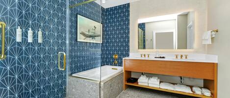 Une salle de bain moderne avec une douche à parois de verre, un meuble-lavabo en bois doté d’un grand miroir et un revêtement mural en carreaux bleus aux motifs géométriques.