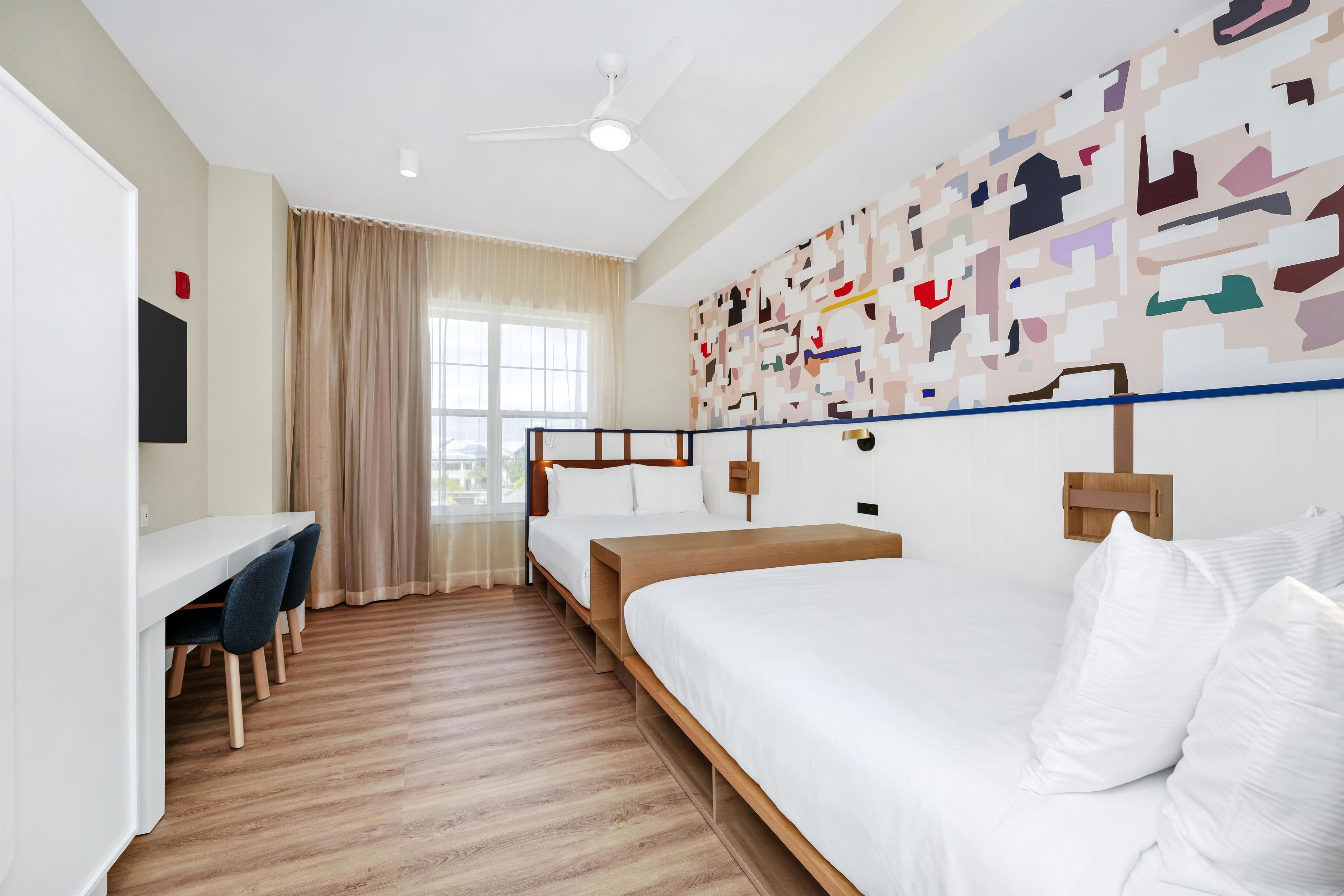 Una camera d'albergo con un letto, una scrivania, sedie e una ventola a soffitto.