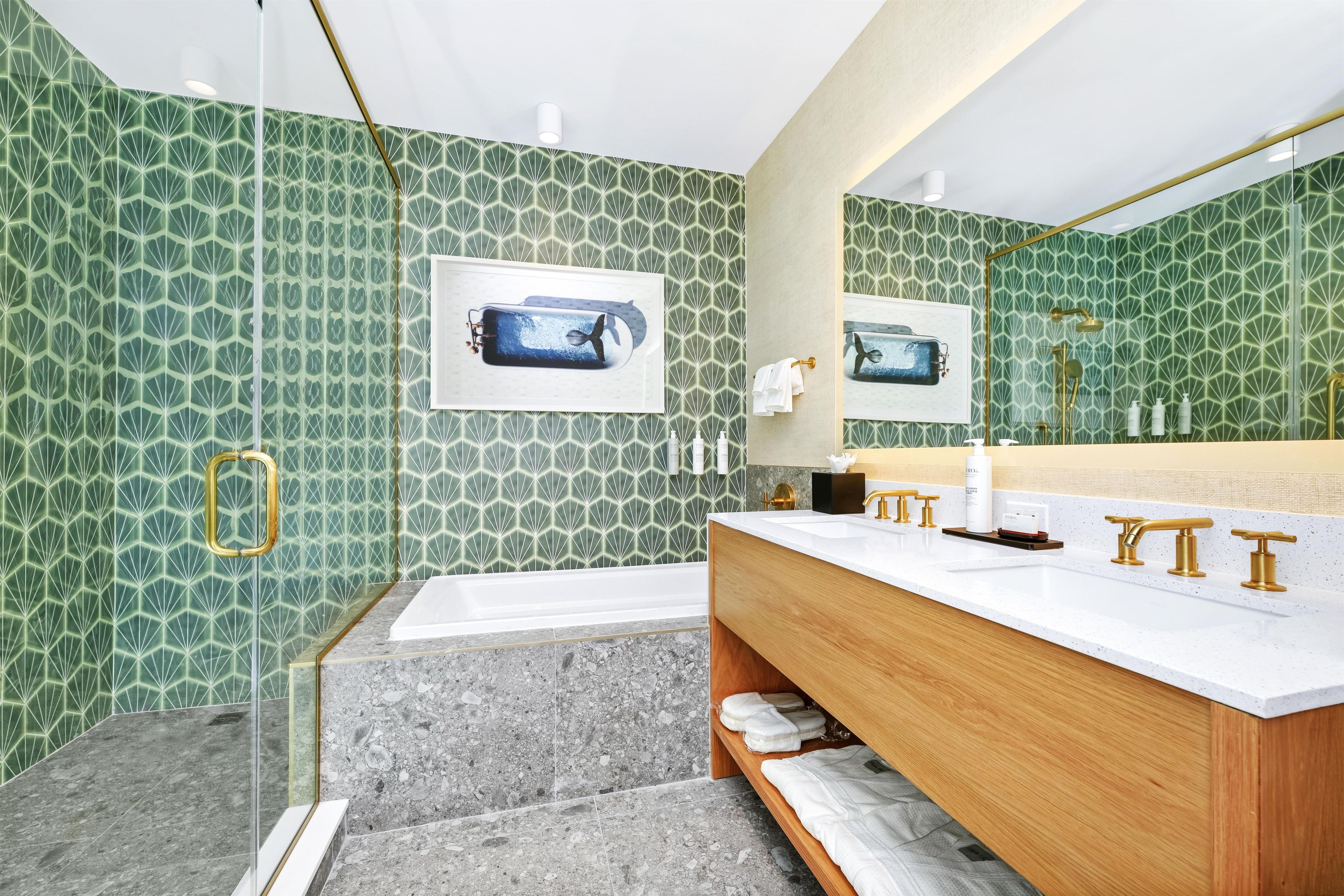 Une salle de bain moderne avec une grande baignoire, un meuble-lavabo avec des accessoires dorés et un mur orné d’un motif vert.