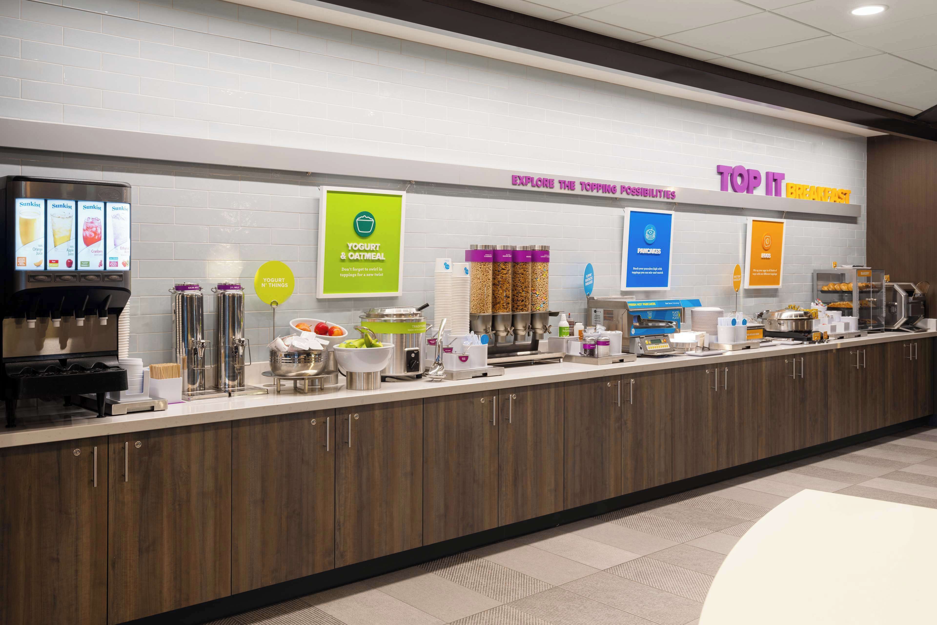 Un bar à petit-déjeuner proposant des yaourts et des options à base de flocons d’avoine, une machine à café et divers autres produits pour le petit-déjeuner.