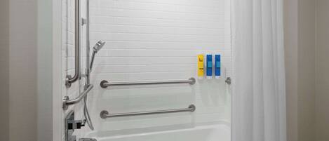 A bathroom with white tiled walls, a bathtub, and a shower with grab bars. There are three bottles of soap on the wall.