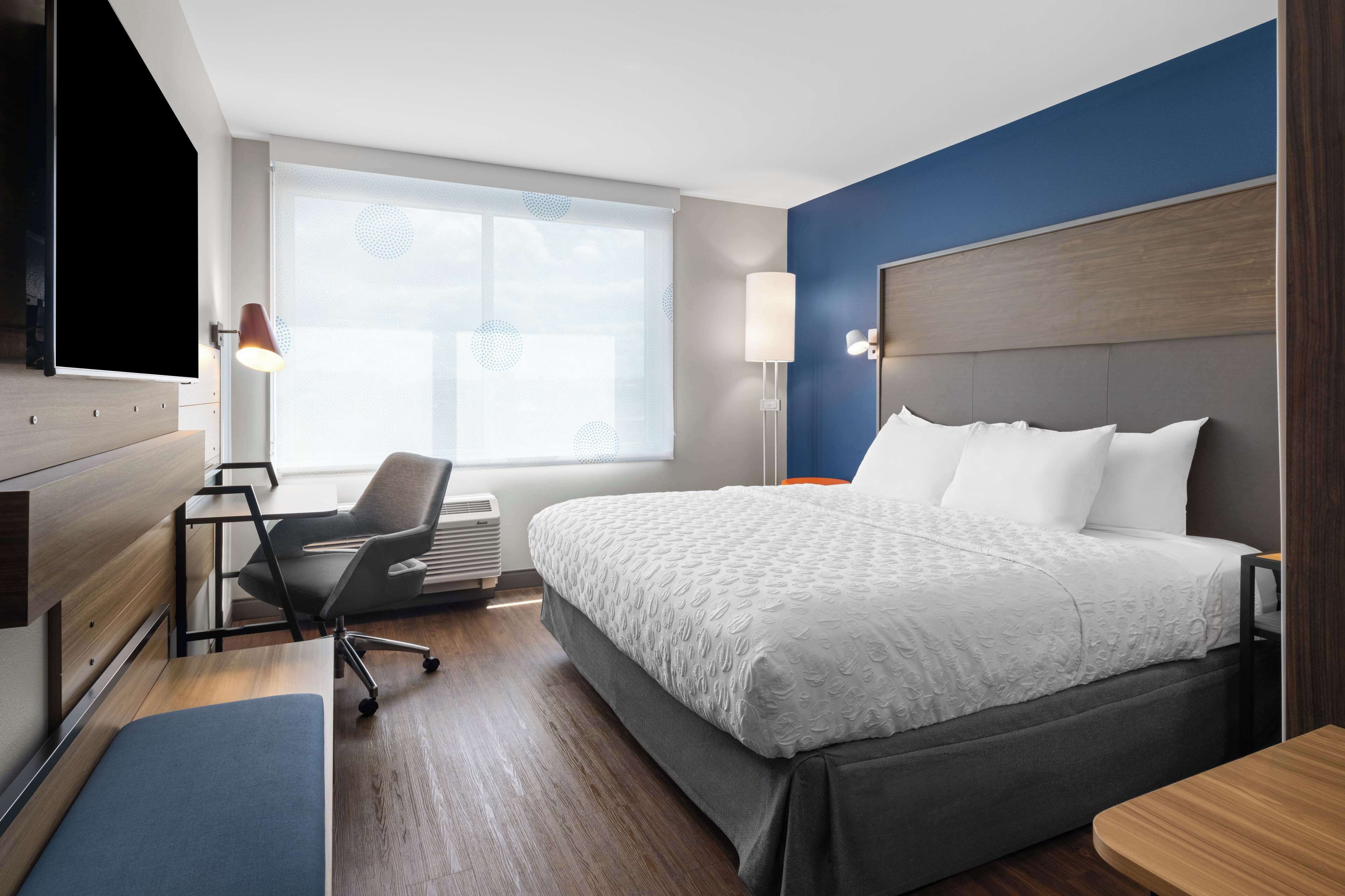 Habitación de hotel con cama, escritorio, silla y un amplio ventanal.