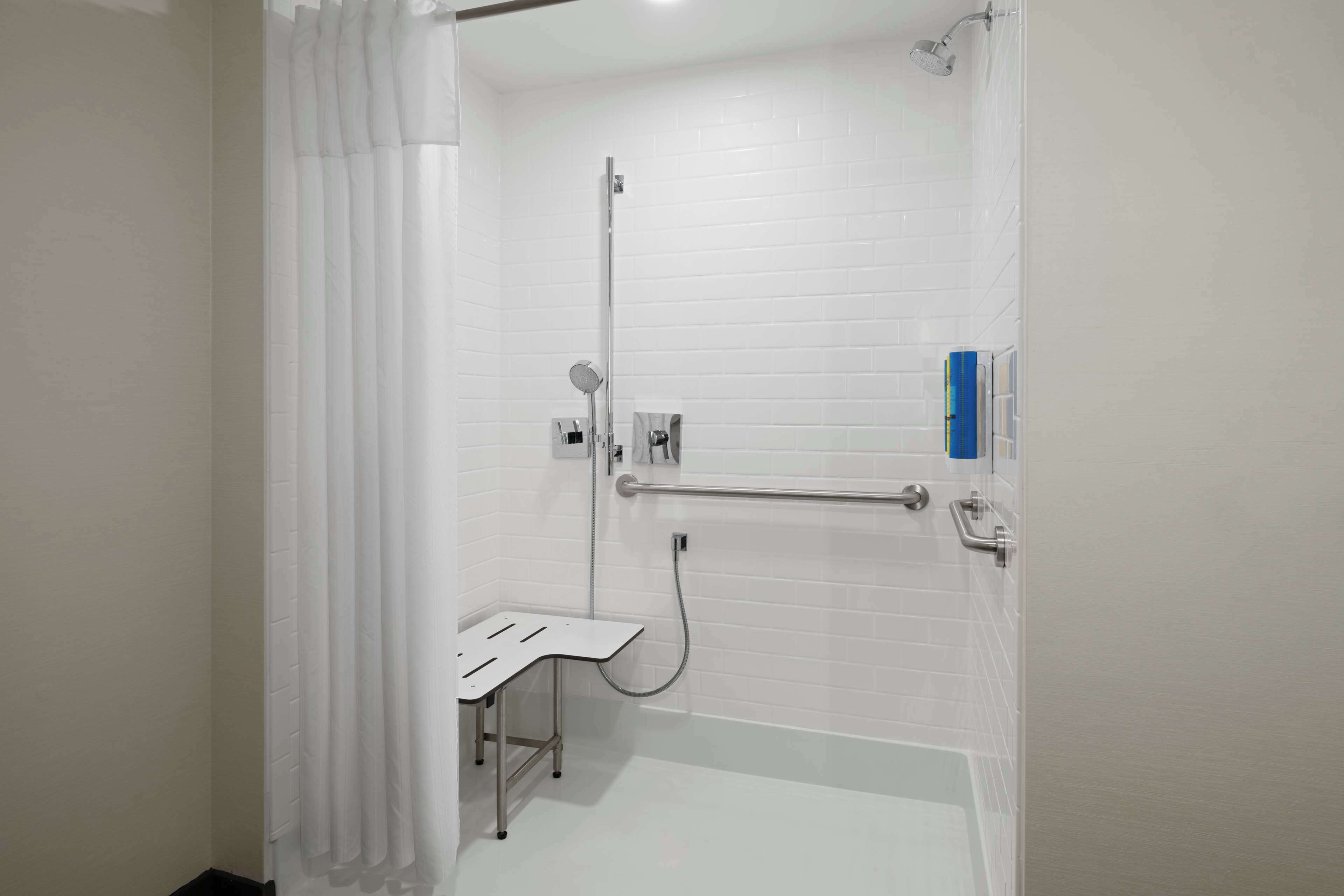 A bathroom with a white shower, a grab bar, and a white bathtub.