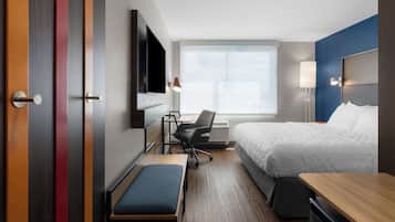 Quarto de hotel com cama, escrivaninha, cadeira, banco, televisão e janela com vista.