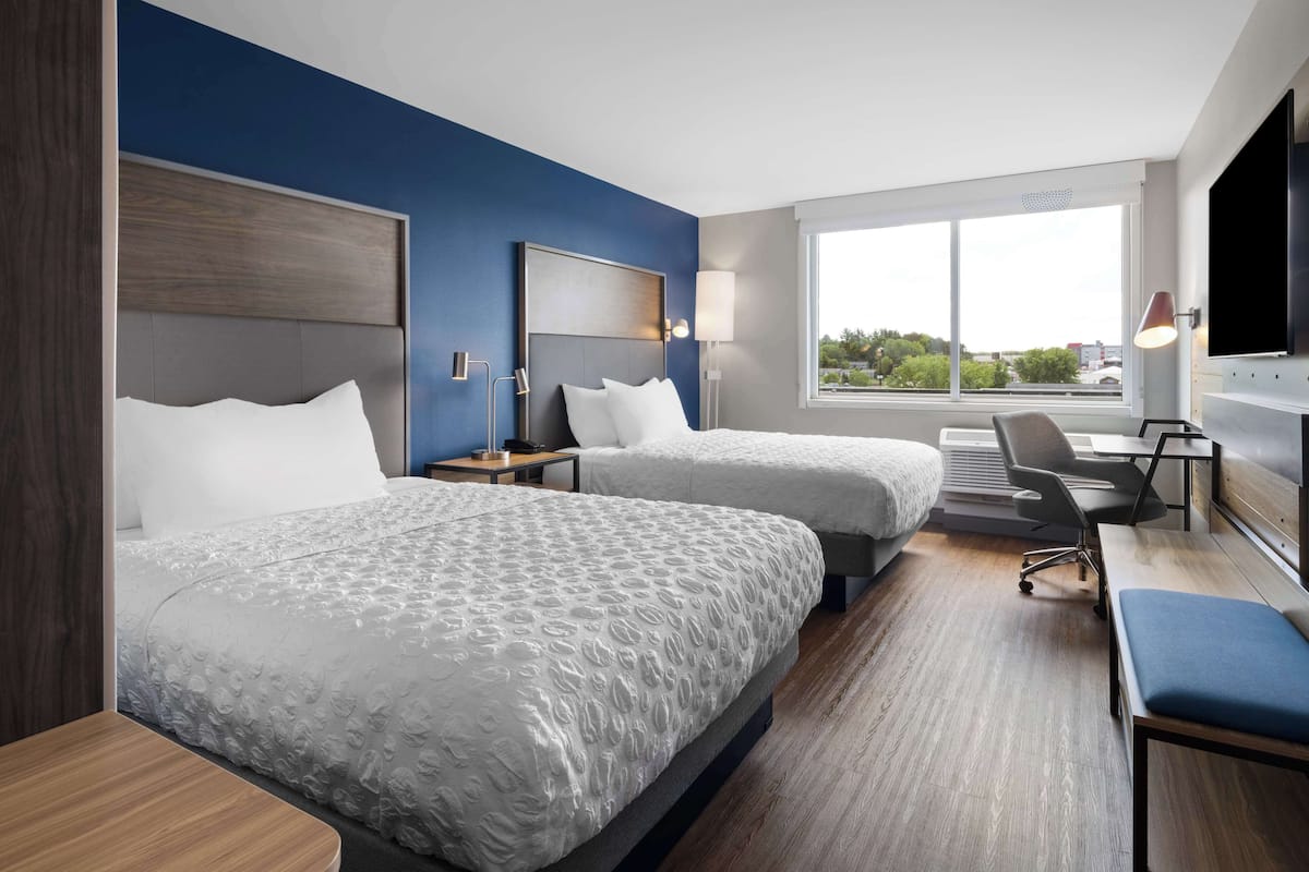 A hotel room with two beds, a desk, and a TV.