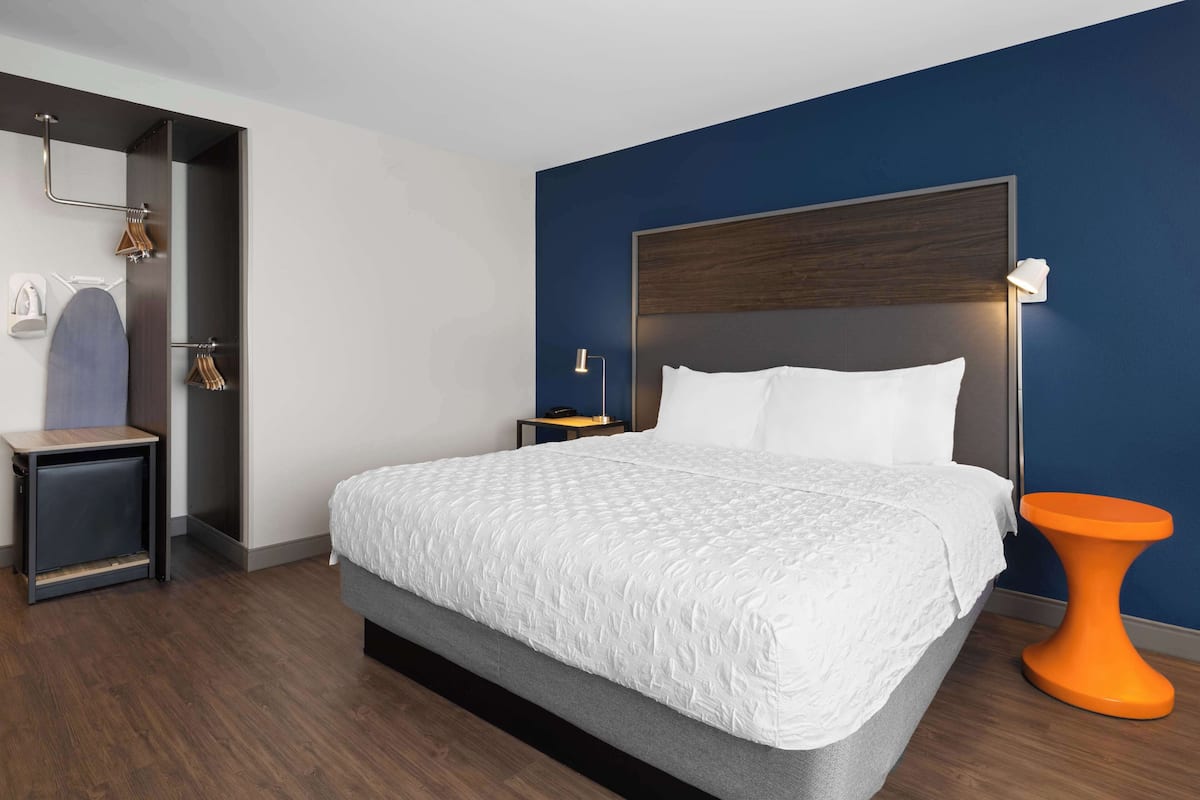 A modern hotel room with a large bed, a nightstand, a small table, and a unique orange side table.