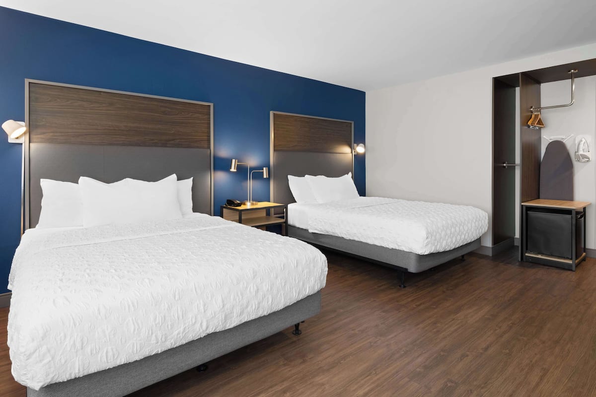 A hotel room with two beds, wooden headboards, bedside tables with lamps, and a wardrobe.