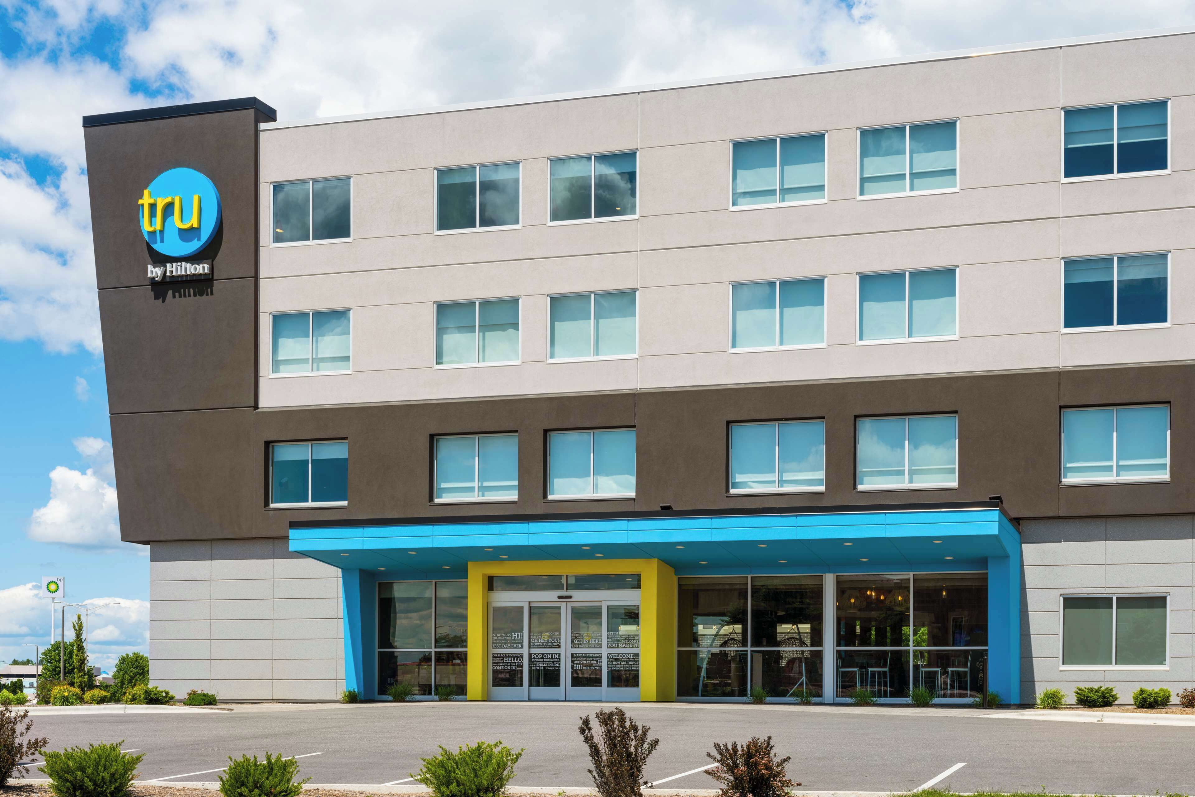 A modern hotel building with a prominent 'tru by Hilton' sign, multiple windows, and a blue entrance area.
