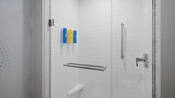 A modern shower with white tiled walls, a glass door, and a metal grab bar.