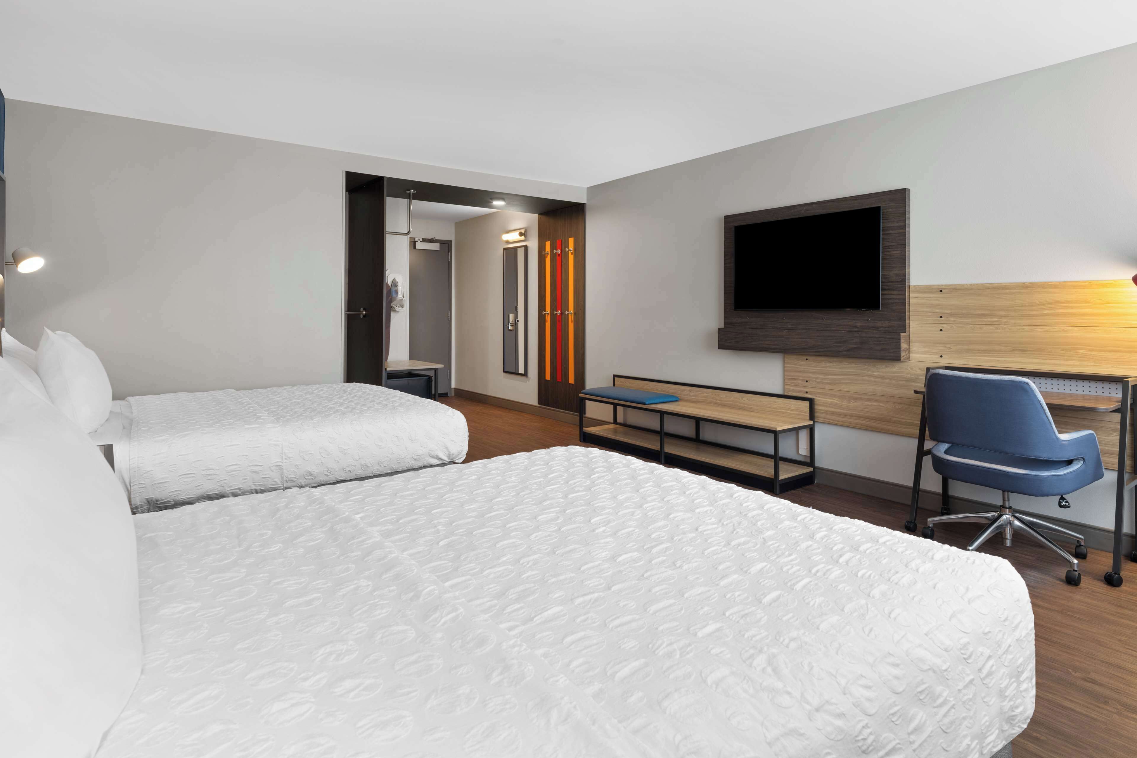 A hotel room with two beds, a desk, a chair, a TV, and a bathroom visible through an open door.