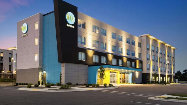 Un hôtel moderne, reconnaissable à son enseigne « tru by Hilton » bien visible, avec de nombreux étages et une entrée bien éclairée.