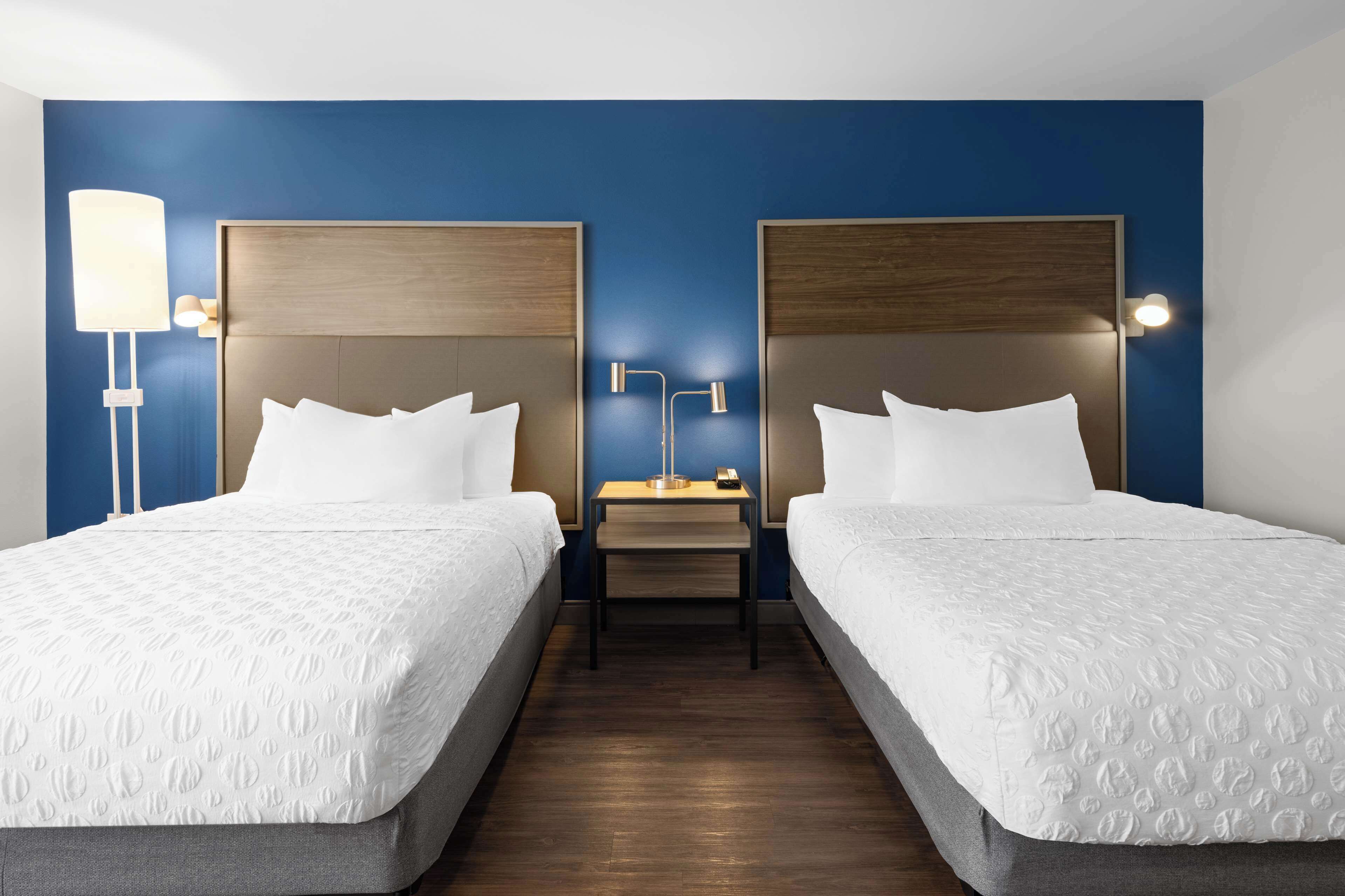 Habitación de hotel con dos camas, una mesita de noche y una lámpara.