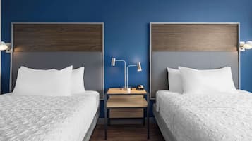 Una habitación de hotel con dos camas, una mesita de noche con lámpara y cabecero de madera.