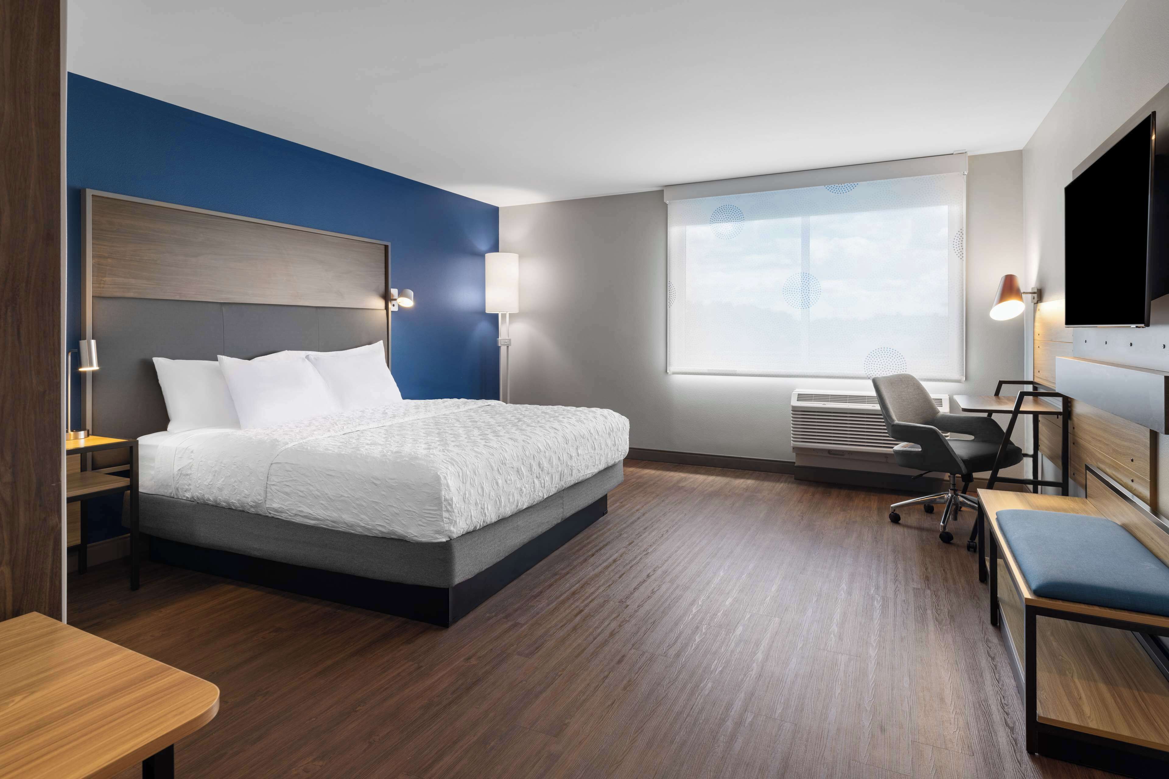 Ein modernes Hotelzimmer mit einem großen Bett, einem Schreibtisch, einem Sessel und einem Fernseher.