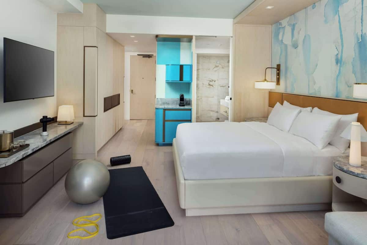 Une chambre d’hôtel moderne équipée d’un grand lit, d’une télévision, d’un bureau avec une lampe et de matériel d’exercice.