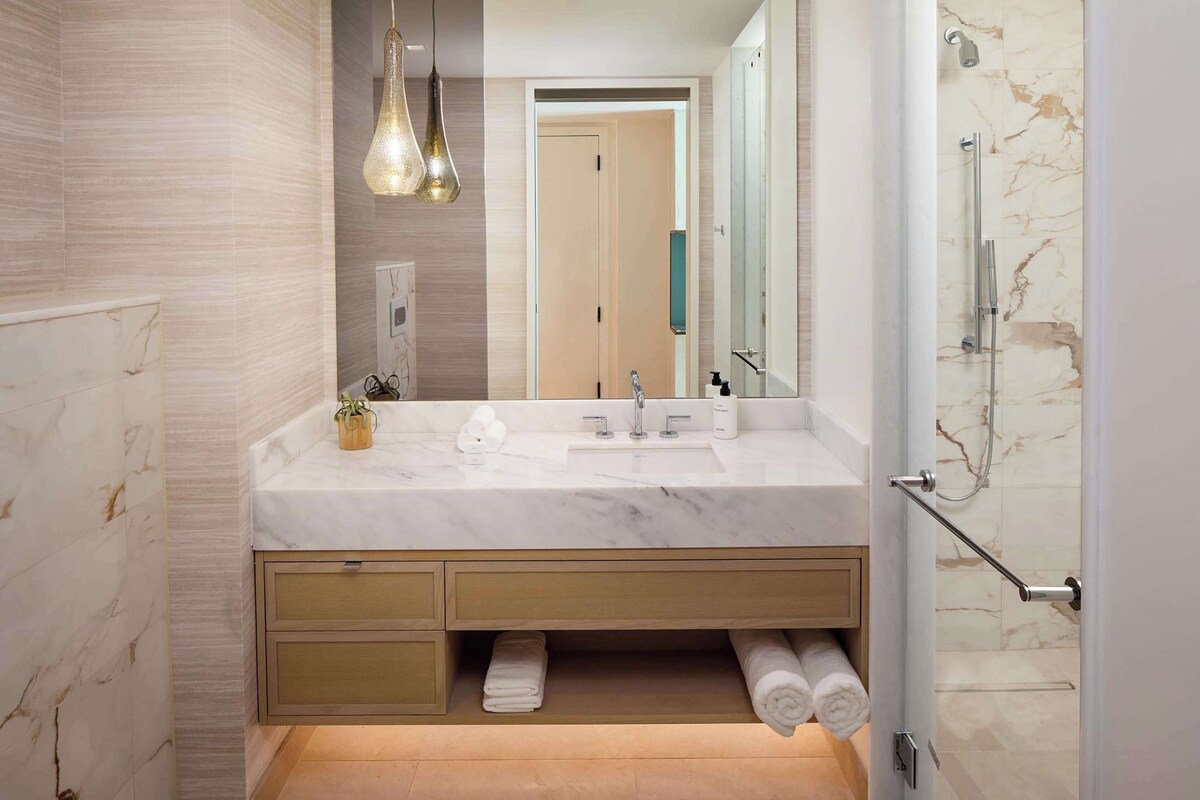 A modern bathroom with a marble vanity, a shower with a glass door, and a towel rack.