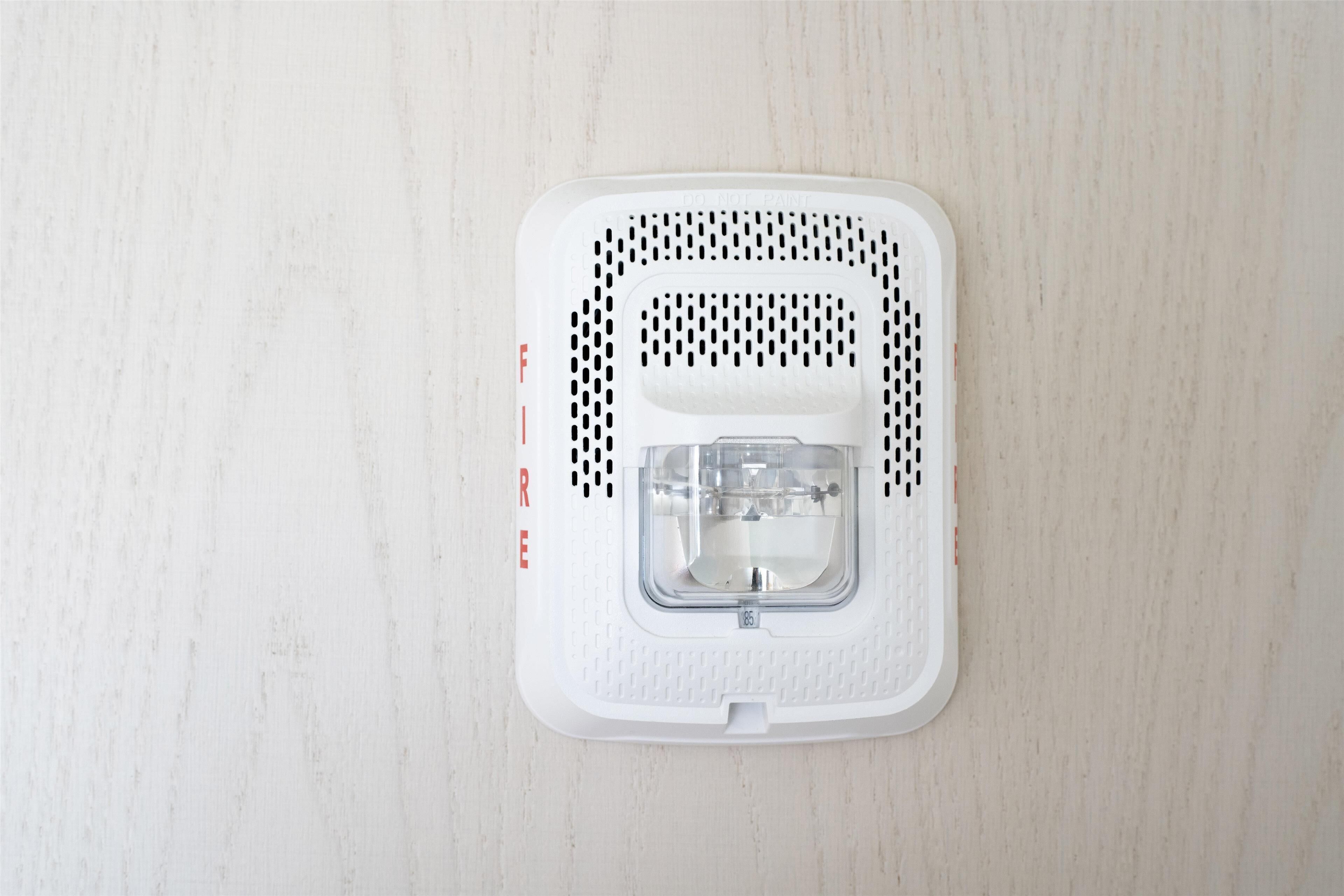 A white smoke detector on a light wooden floor.