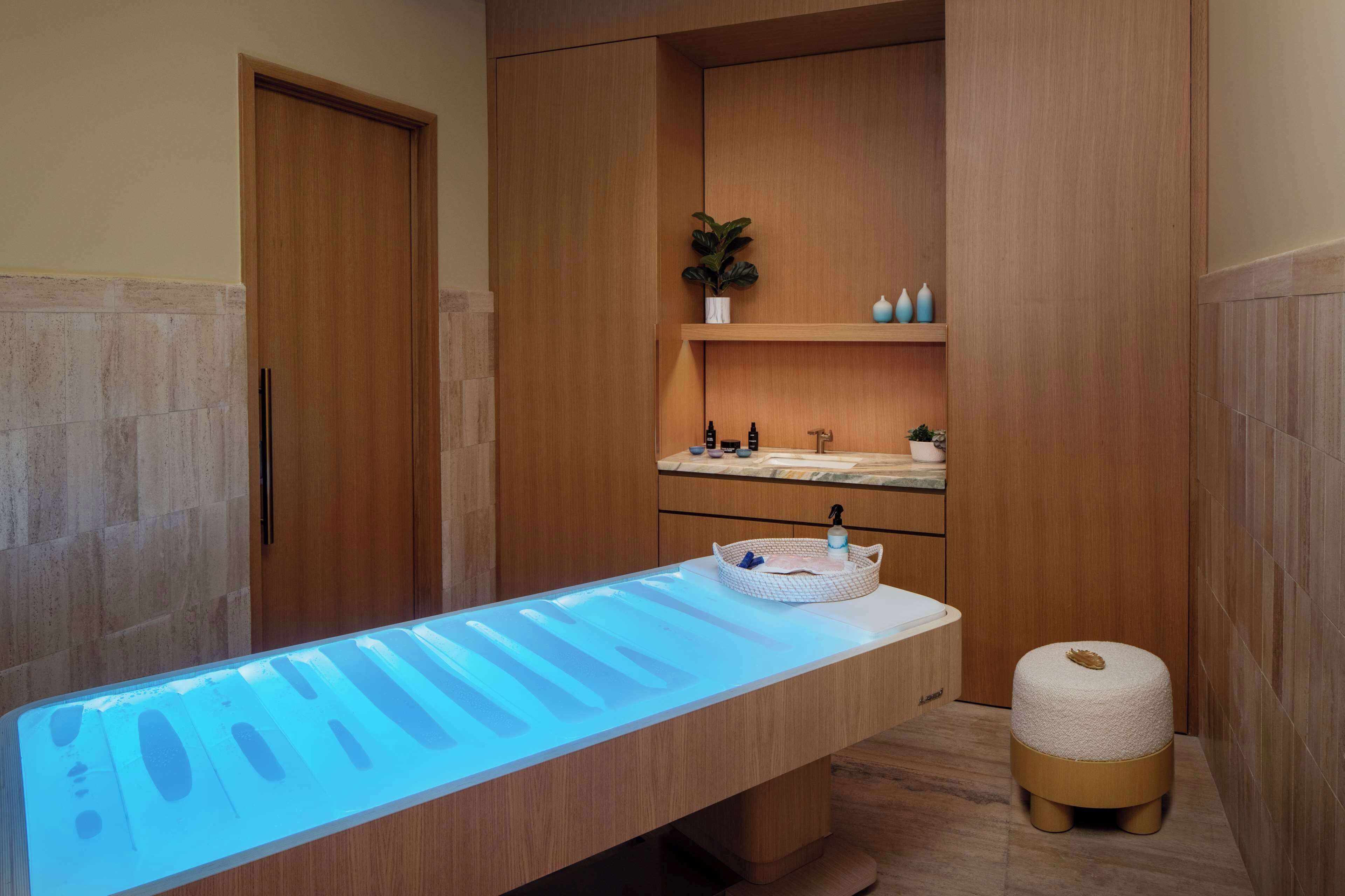 A modern bathroom with a long, illuminated countertop, wooden cabinets, and a small stool.