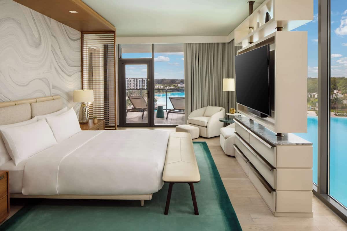 Une chambre d’hôtel moderne dotée d’un grand lit, d’une télévision à écran plat, d’un balcon avec vue sur la piscine et d’une porte-fenêtre coulissante.