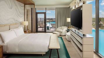 A modern hotel room with a large bed, a flat-screen TV, a balcony with a pool view, and a sliding glass door.