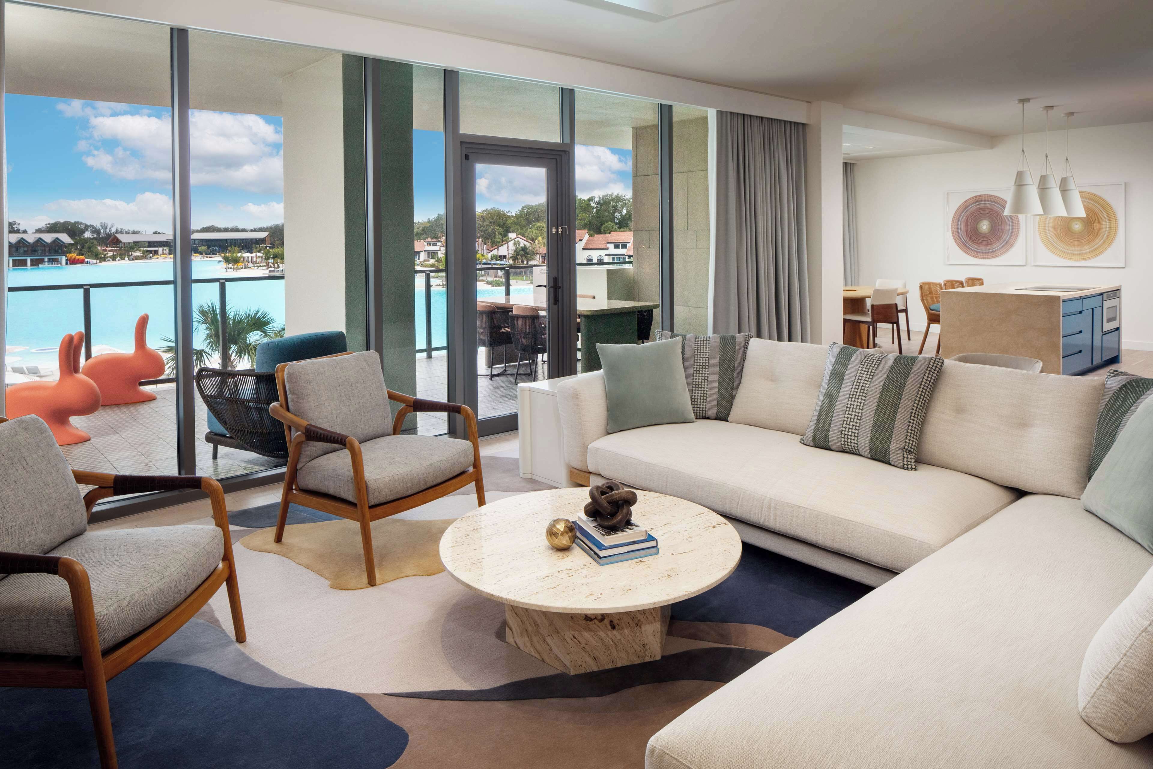 Una sala de estar moderna con un sofá grande, sillones, una mesa de centro y vistas a una piscina y edificios.