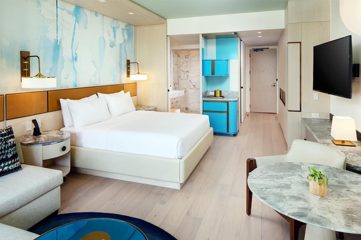 Une chambre d’hôtel moderne dotée d’un grand lit, d’un coin salon, d’une petite cuisine et d’une télévision.