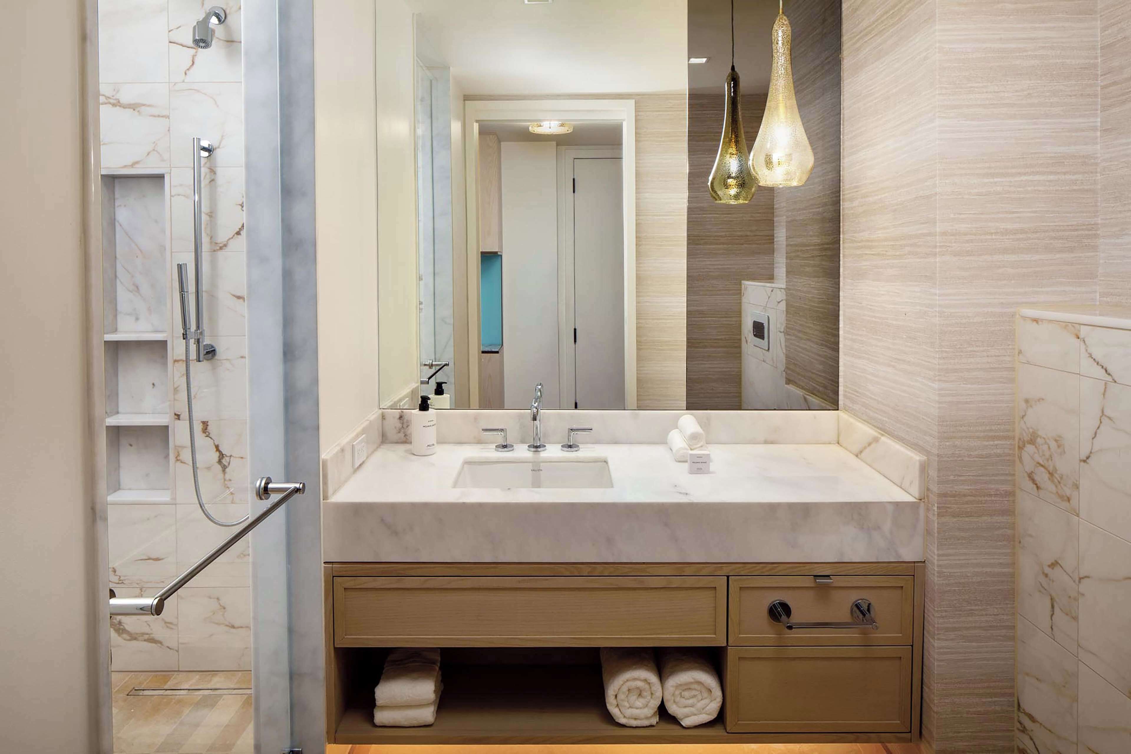 A modern bathroom with a marble sink, a glass shower enclosure, and a large mirror.