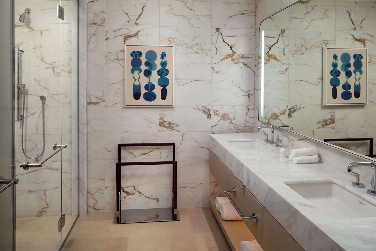 A modern bathroom with marble walls, a large mirror, and a shower with glass doors.