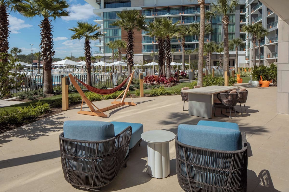 Une terrasse d’hôtel avec des meubles en osier, un hamac et un espace piscine.