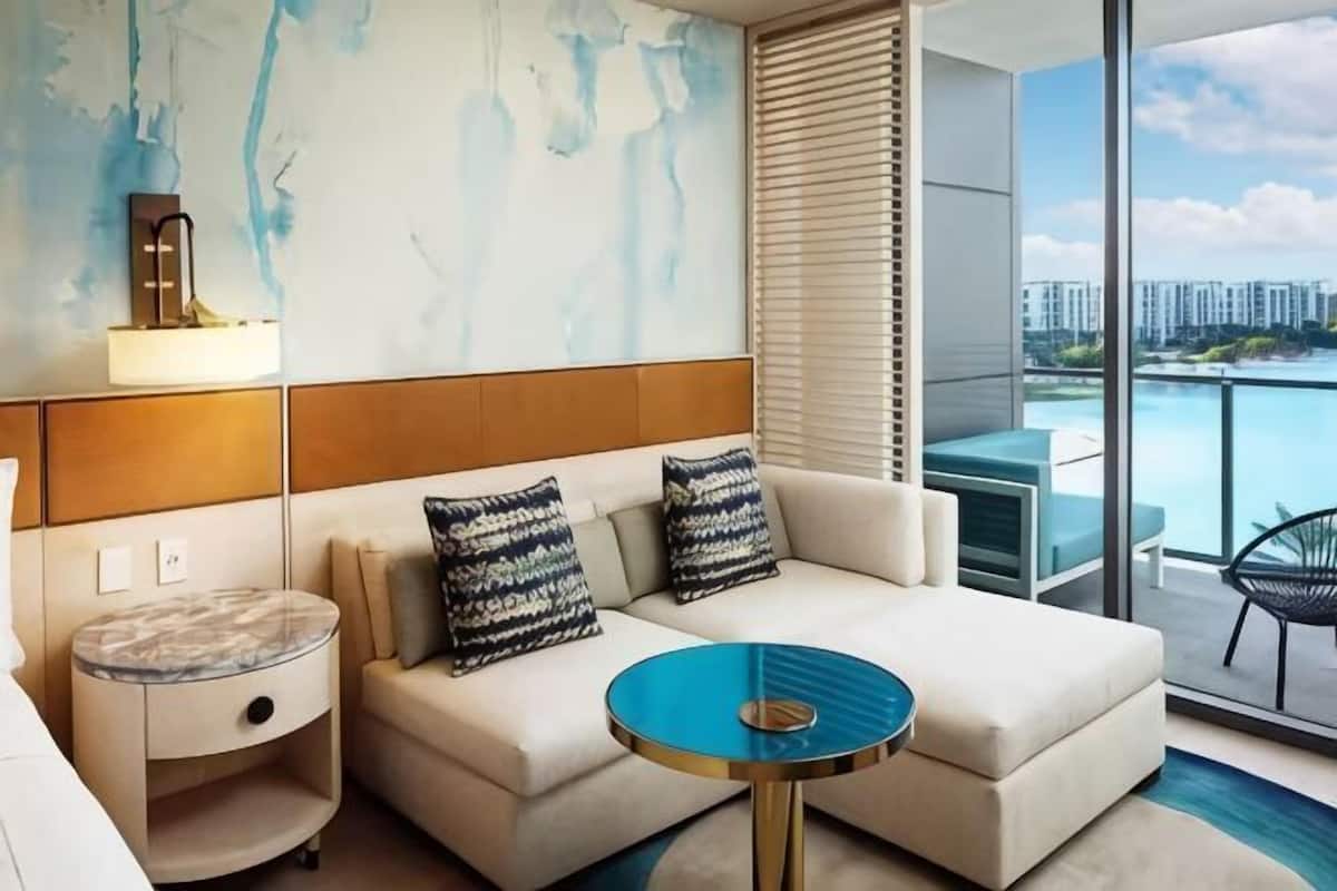 Une chambre d’hôtel moderne, dotée d’un canapé, d’une petite table ronde, d’une lampe fixée au mur et offrant une vue sur le paysage urbain grâce à de grandes fenêtres.
