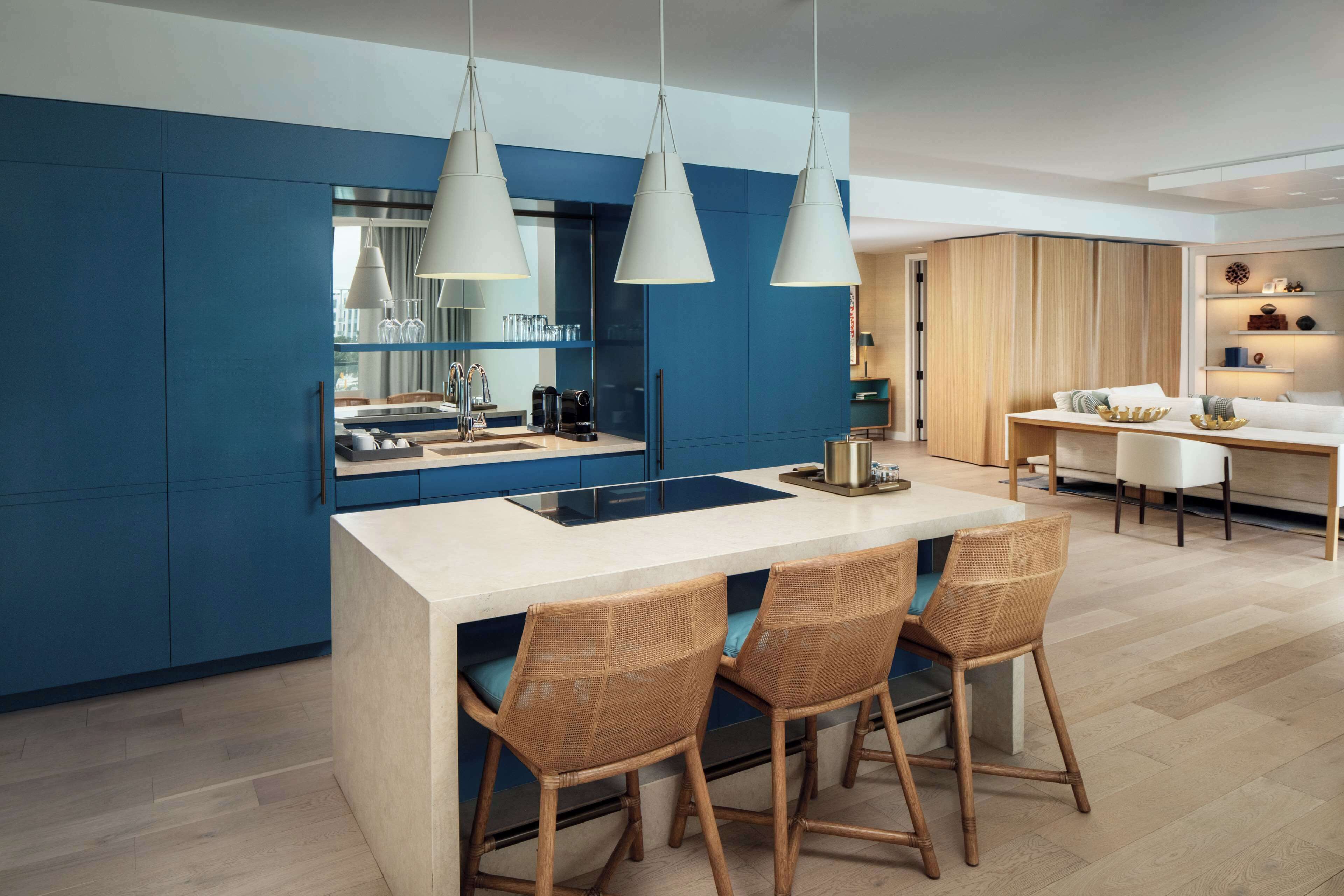 Una cucina moderna con mobili blu, un'isola centrale con sgabelli da bar, illuminazione a sospensione e un'area pranzo con tavolo e sedie bianche.